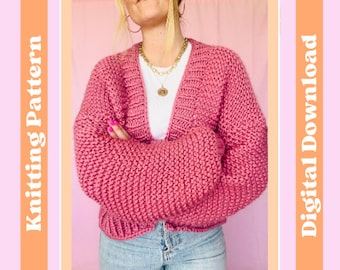 Puede incluir: Un cárdigan de punto rosa con cuello en V y mangas largas. El cárdigan se muestra en una modelo con una camisa blanca debajo y pantalones vaqueros azules.