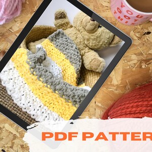 May include: A digital tablet displaying a PDF pattern for a striped knitted blanket in white, yellow, and gray. The blanket is in a woven basket with a teddy bear on top. The text "PDF PATTERN" is on a white background with orange text.