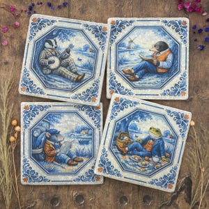 May include: Set of four square ceramic coasters with blue and white floral border designs. Each coaster features a different anthropomorphic animal in a pastoral scene. The animals include a badger, mole, mouse, and frog.