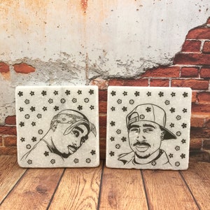 May include: Two square white coasters with black floral patterns and black and white images of the rapper Tupac Shakur.