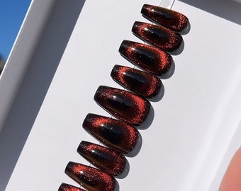 May include: Set of ten coffin-shaped false nails with a red and black cat eye glitter finish.