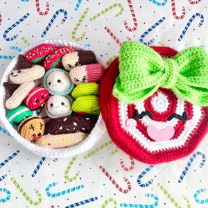 May include: A white crocheted basket filled with various crocheted food items, including a donut, a hot dog, a macaron, and a watermelon slice. The basket is next to a red and white crocheted candy cane with a green bow.