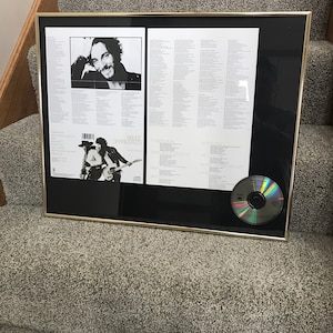 May include: Framed Bruce Springsteen album art and CD. The frame has a gold border and a black mat. The artwork includes a black and white photo of Springsteen and song lyrics. A CD is in the lower right corner.