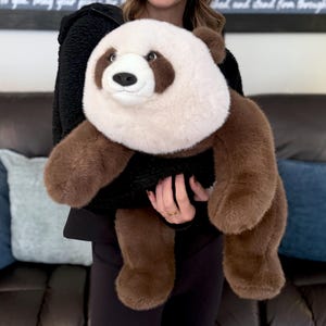 May include: A plush panda bear toy with a white head and chest, brown arms, legs, and ears, and a black body. The panda has a friendly expression and is made of soft, fuzzy material.