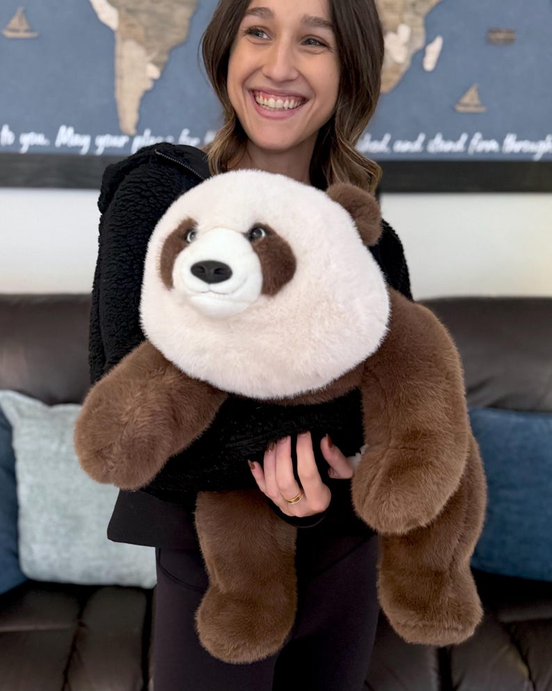 May include: A plush panda bear toy with a white head and chest, brown arms, legs, and ears, and a black body. The panda has a friendly expression and is made of soft, fuzzy material.