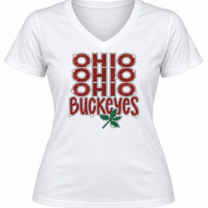 May include: A white V-neck t-shirt featuring a graphic design made of red rhinestones that spells out OHIO three times vertically and the word BUCKEYES below it, accompanied by a small green rhinestone leaf icon at the bottom center of the design.