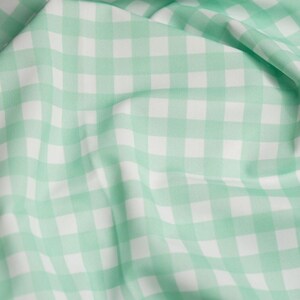K&ouml;nnte beinhalten: Ein Stoff mit einem klassischen Vichy-Karo-Muster, bestehend aus abwechselnden Quadraten in sanftem Mintgr&uuml;n und klarem Wei&szlig;. Das Material ist in Falten gelegt, wodurch das gleichm&auml;&szlig;ige Karomuster auf der gesamten Textiloberfl&auml;che sichtbar wird.