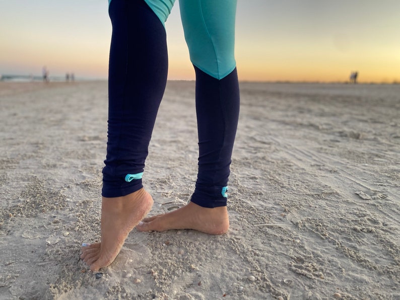 K&ouml;nnte beinhalten: Leggings mit einem Color-Blocking-Design, bestehend aus einem hellblauen oberen Teil und einem dunkel marineblauen unteren Teil. Die Leggings haben kleine hellblaue Schlaufen an den Kn&ouml;cheln und einen kleinen rechteckigen Aufn&auml;her am linken Bein.