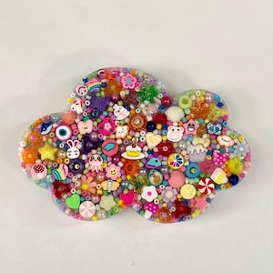 May include: A cloud-shaped resin piece filled with a dense arrangement of colorful beads and charms. The surface features various shapes including small animals, flowers, stars, hearts, food items, and geometric beads in a wide spectrum of colors.