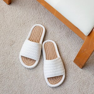 May include: A pair of white crocheted slippers with a tan woven sole. The slippers are on a light brown shag rug.