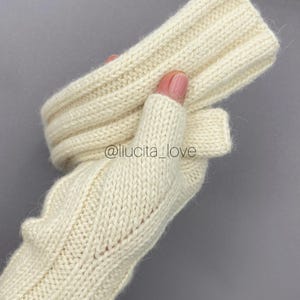 May include: Cream-coloured fingerless gloves with a ribbed cuff and a cable knit design on the hand. The gloves are made of a soft, textured yarn. The text "@liucita_love" is visible.