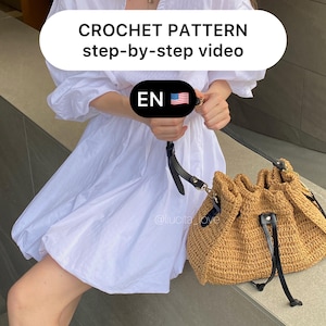 Puede incluir: Un vestido blanco y un bolso de paja tejida con detalles de cuero negro. El bolso tiene un cierre de cordón. El texto en la imagen dice "CROCHET PATTERN step-by-step video" y "EN".