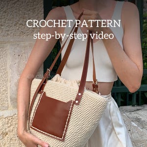 May include: A cream-colored crochet tote bag with brown leather accents. The bag features a brown leather pocket and handles, with the text "CROCHET PATTERN step-by-step video".