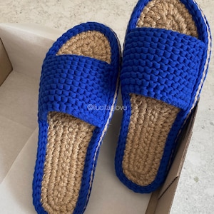 Puede incluir: Un par de zapatillas de crochet azul y marrón. Las zapatillas tienen un diseño sencillo y están hechas con un hilo grueso.