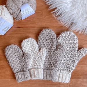 May include: Three pairs of crocheted mittens in beige and white. The mittens are made with a textured stitch and have a contrasting cuff.