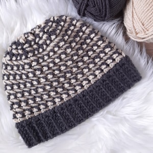 Puede incluir: Un gorro de punto gris y beige con un patr&oacute;n texturizado. El gorro est&aacute; hecho con dos colores de hilo diferentes.