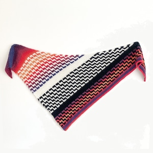 May include: A triangular crocheted shawl with a colorful ombre pattern in shades of red, orange, purple, and white. The shawl has a black and white zig-zag pattern in the center.