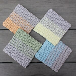May include: Four crocheted squares in different colors: light peach, light green, light blue, and light yellow. Each square has a two-toned design with a lighter color in the center and a darker color around the edges.