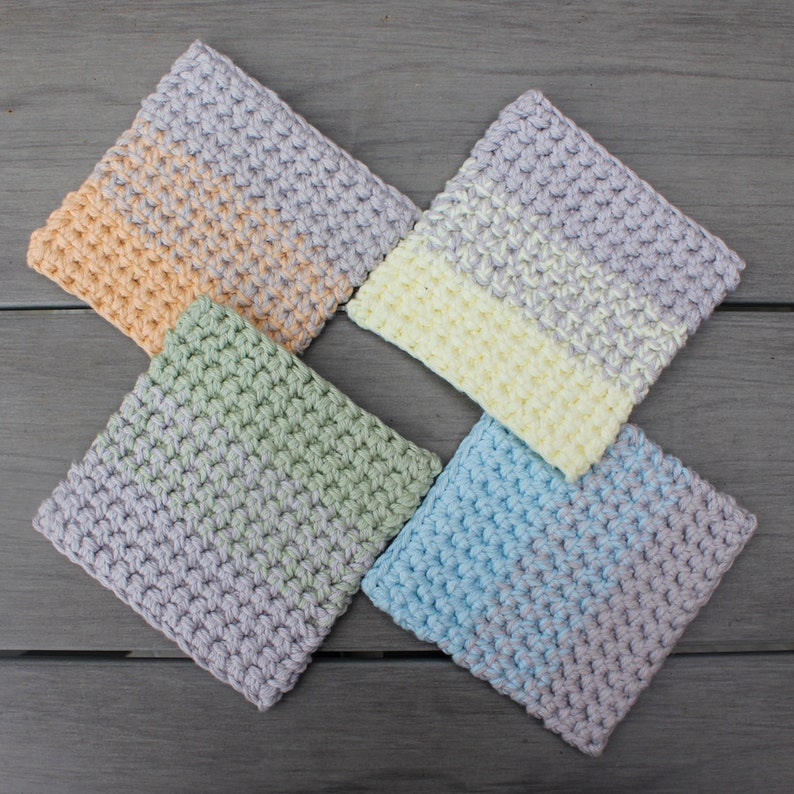 May include: Four crocheted squares in different colors: light peach, light green, light blue, and light yellow. Each square has a two-toned design with a lighter color in the center and a darker color around the edges.
