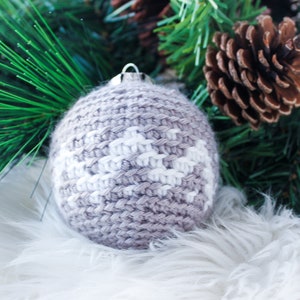 May include: A spherical crochet ornament featuring a light brown and white geometric pattern. The round, textured yarn decoration has a silver-colored metal cap at the top for hanging, showcasing intricate knit stitches throughout the surface.