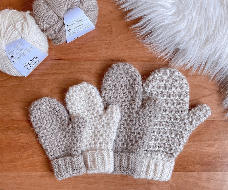 May include: Three pairs of crocheted mittens in beige and white. The mittens are made with a textured stitch and have a contrasting cuff.