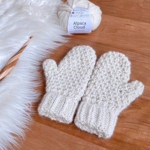 May include: A pair of crocheted mittens in a cream color. The mittens are made with a textured stitch and have a ribbed cuff. The yarn used is Alpaca Cloud DK weight.