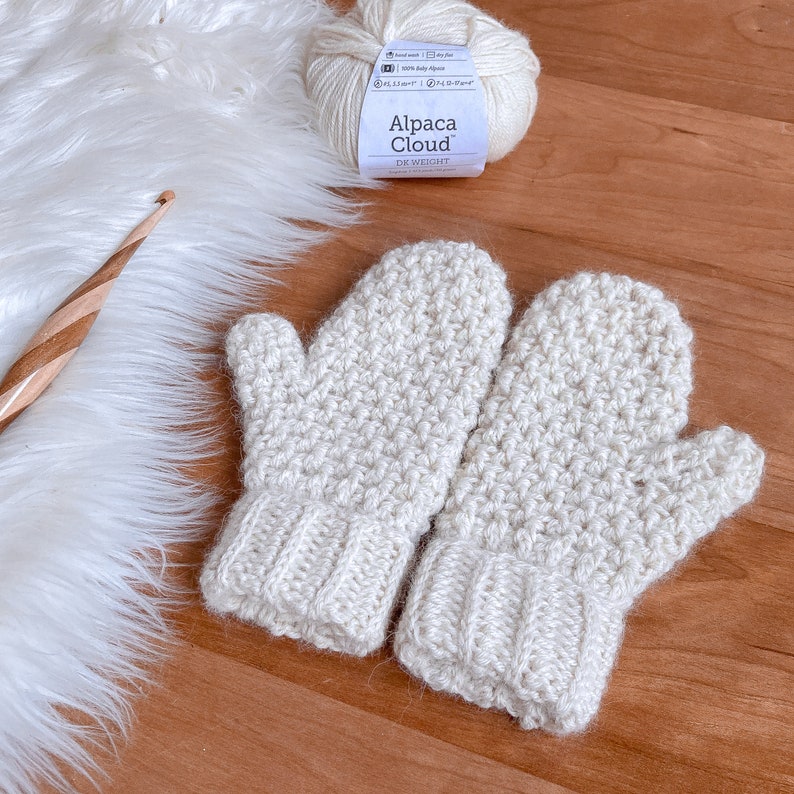 May include: A pair of crocheted mittens in a cream color. The mittens are made with a textured stitch and have a ribbed cuff. The yarn used is Alpaca Cloud DK weight.