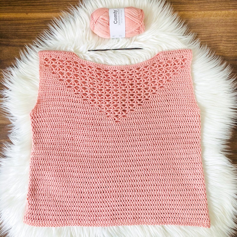 May include: A pink crochet top with a lacy pattern around the neckline. The top is sleeveless and has a relaxed fit.