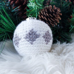 May include: A spherical Christmas ornament featuring white yarn crochet work with a repeating gray diamond pattern. The ornament has a silver-colored metal cap at the top for hanging, showcasing a textured, handmade knit construction.