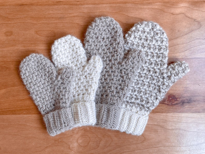 May include: Three crocheted mittens in beige and white. The mittens are made with a textured stitch and have a simple cuff.