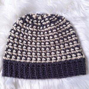 Puede incluir: Un gorro de punto de color gris y crema con un patr&oacute;n texturizado. El gorro tiene un borde doblado.
