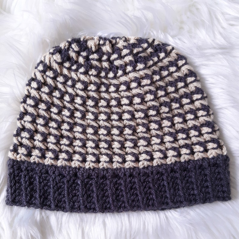 Puede incluir: Un gorro de punto de color gris y crema con un patr&oacute;n texturizado. El gorro tiene un borde doblado.