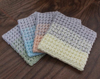 May include: Four crocheted coasters in different color combinations. The coasters are made with a textured stitch and feature a two-tone design. The colors include light green, light blue, peach, and cream.