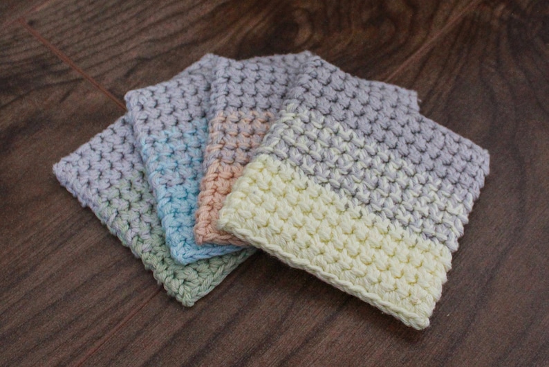 May include: Four crocheted coasters in different color combinations. The coasters are made with a textured stitch and feature a two-tone design. The colors include light green, light blue, peach, and cream.