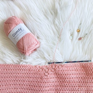 May include: A pink ball of yarn labeled "Comfy Fingering Weight" with a crochet hook and a pink crocheted blanket.