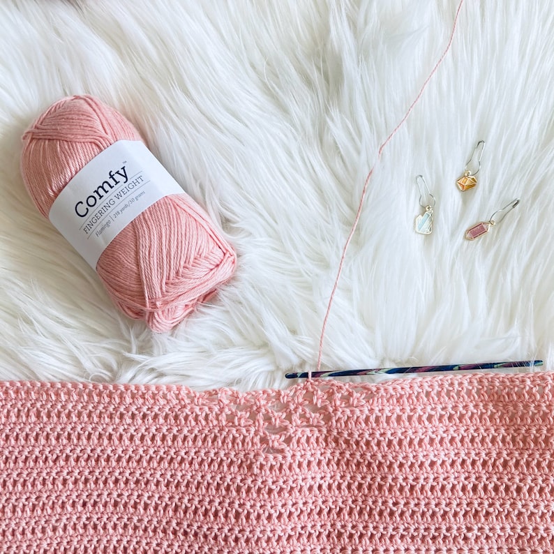 May include: A pink ball of yarn labeled "Comfy Fingering Weight" with a crochet hook and a pink crocheted blanket.