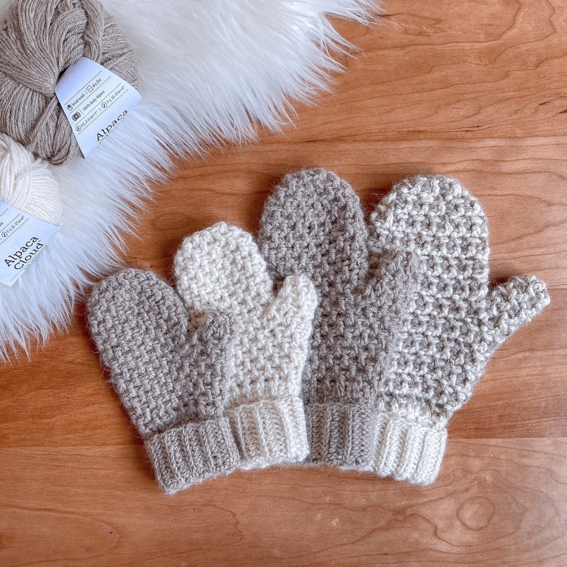 May include: Three pairs of crocheted mittens in beige and white. The mittens are made with a textured stitch and have a simple cuff.