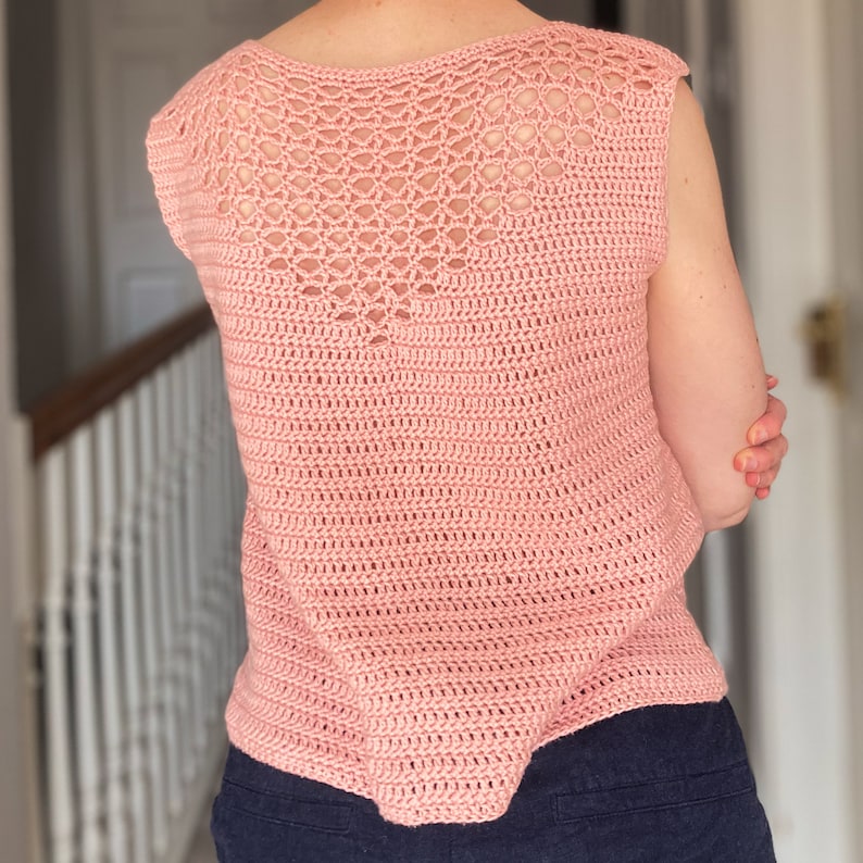 May include: A pink crochet top with a delicate openwork design on the back. The top has a sleeveless design and a relaxed fit.