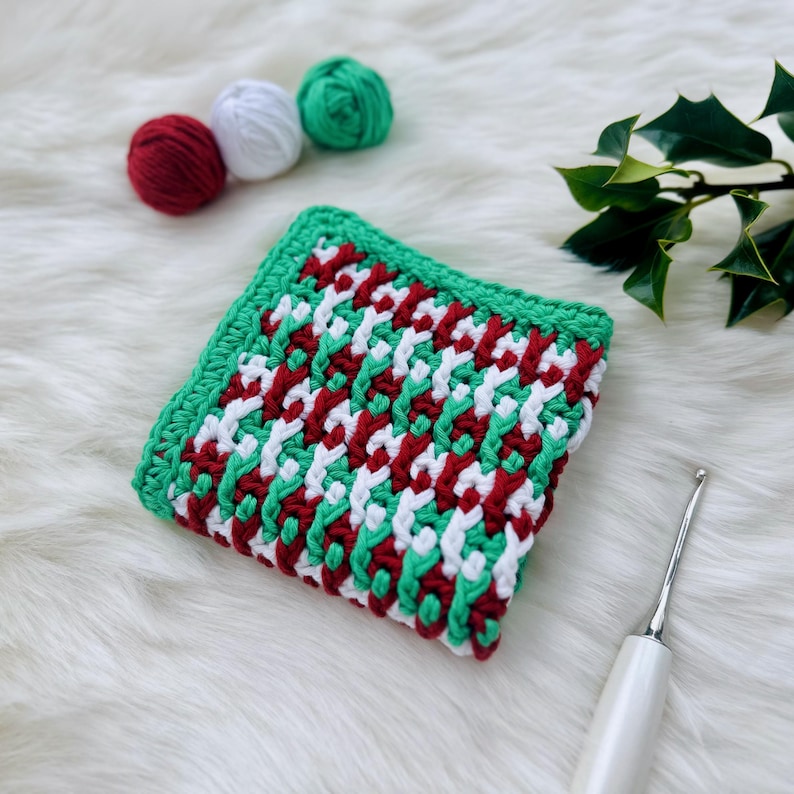 May include: A crocheted dishcloth in red, white, and green. The dishcloth is made with a simple stitch pattern and has a square shape.