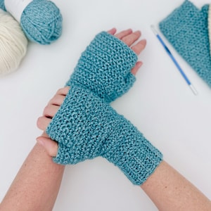 May include: A pair of teal blue crocheted fingerless gloves. The gloves are made with a textured stitch and are shown on a person's hands.
