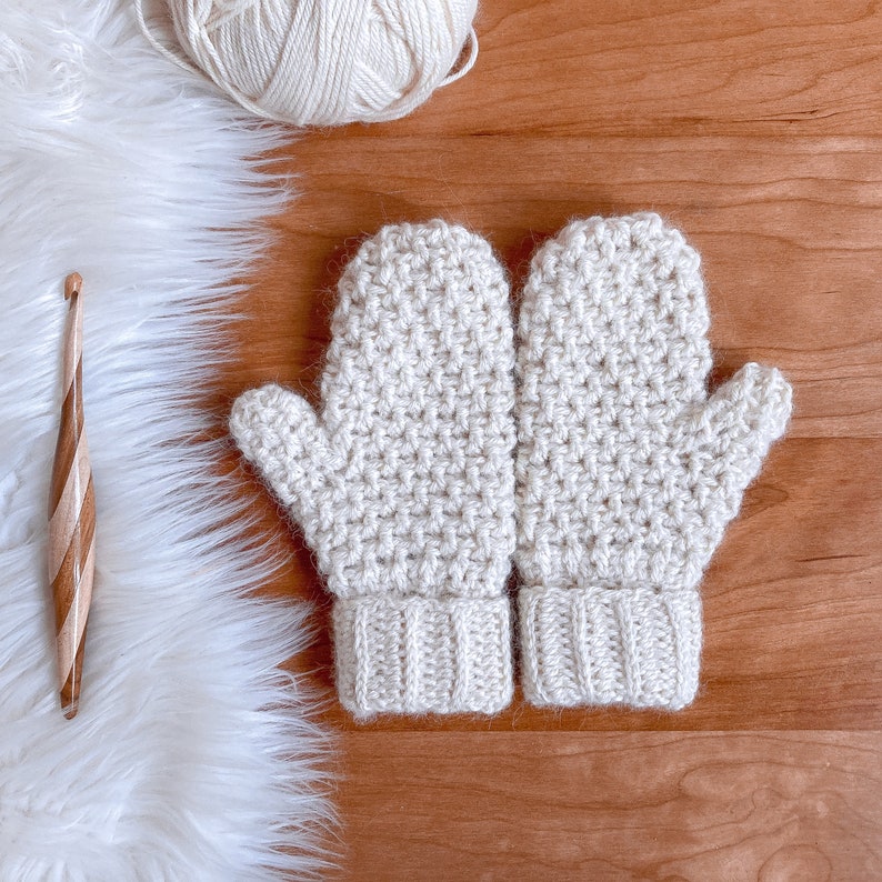 May include: A pair of crocheted mittens in a cream color. The mittens have a textured stitch pattern and are made with a soft yarn.