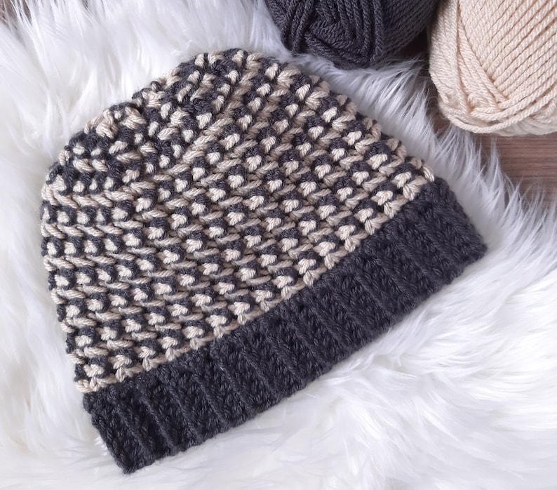 Puede incluir: Un gorro de punto gris y beige con un patr&oacute;n texturizado. El gorro est&aacute; hecho con dos colores de hilo diferentes.
