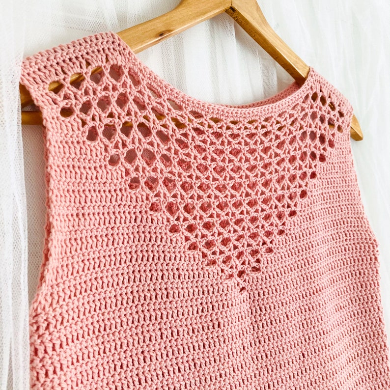 May include: A pink crocheted sleeveless top with a delicate openwork design around the neckline.