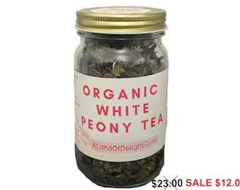 May include: A glass jar filled with loose leaf organic white peony tea. The jar has a gold lid and a white label with the text "ORGANIC WHITE PEONY TEA" and "AlandOfDelight.com". The text "$23.00 SALE $12.00" is printed below the jar.