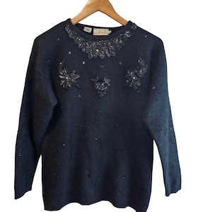 May include: A dark gray sweater with long sleeves, embellished with sequins and beaded floral designs. The neckline is adorned with a beaded collar. The brand name "Rafaella" is visible on the label.