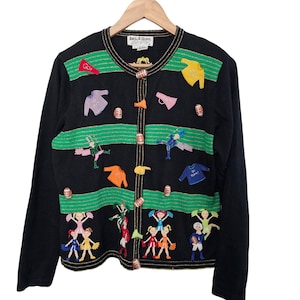 May include: Black cardigan with green and gold accents, featuring football and cheerleader appliqués. The sweater has long sleeves and a button-up front. The design includes footballs, cheerleaders, and the word "GO".
