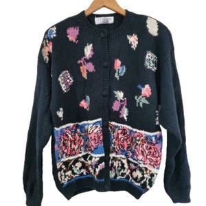 May include: A black cardigan sweater with a floral pattern. The cardigan has a button-up front and long sleeves. The floral pattern is in shades of pink, blue, green, and white.