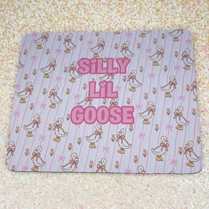 May include: A rectangular mousepad with a repeating pattern of cartoon geese wearing bows and shoes, set against a light pink striped background. The words "Silly Lil Goose" are in pink bubble letters.