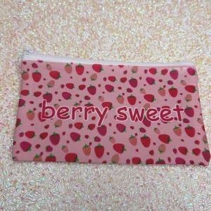 May include: Pink zippered pouch with a strawberry pattern and the words "berry sweet" in a cursive font. The pouch is covered in red and pink strawberries of various sizes.
