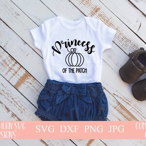 May include: White baby onesie with black text that reads "Princess of the Patch" with a pumpkin graphic. The onesie is on a white wooden surface with a pair of brown baby shoes.